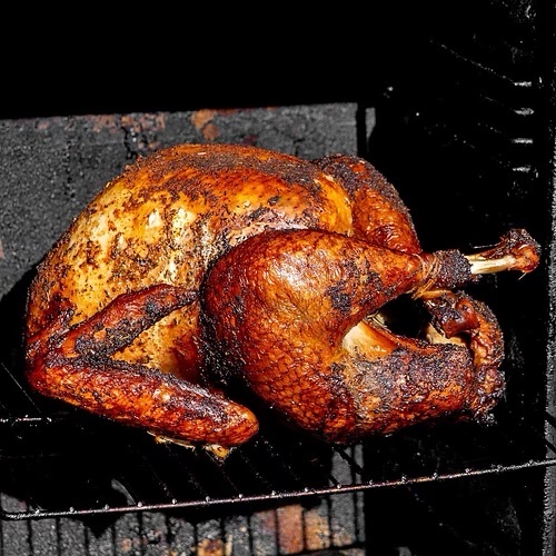A whole smoked turkey with a dark, peppery crust on the smoker grate